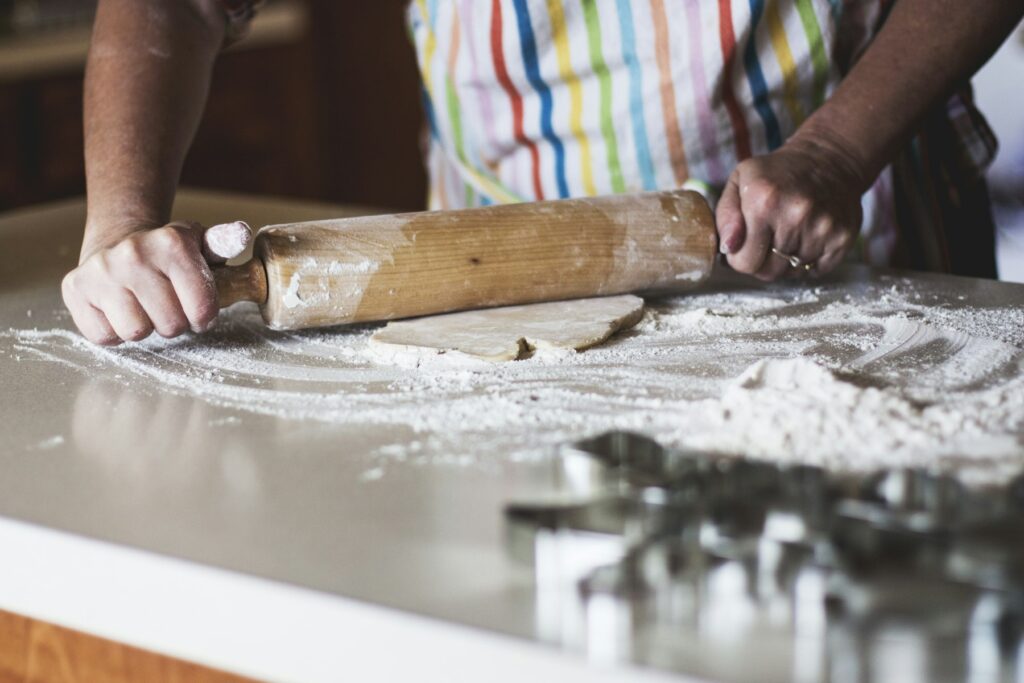 Home baker rolling out dough with a wooden rolling pin and cookie cutters