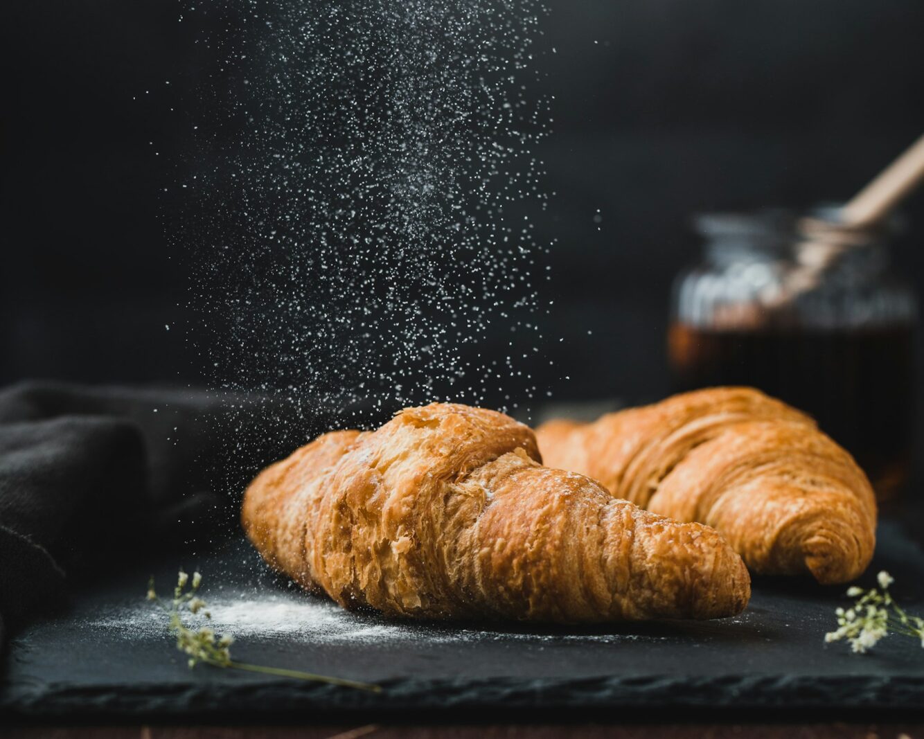 A golden croissant dusted with flour on a dark surface