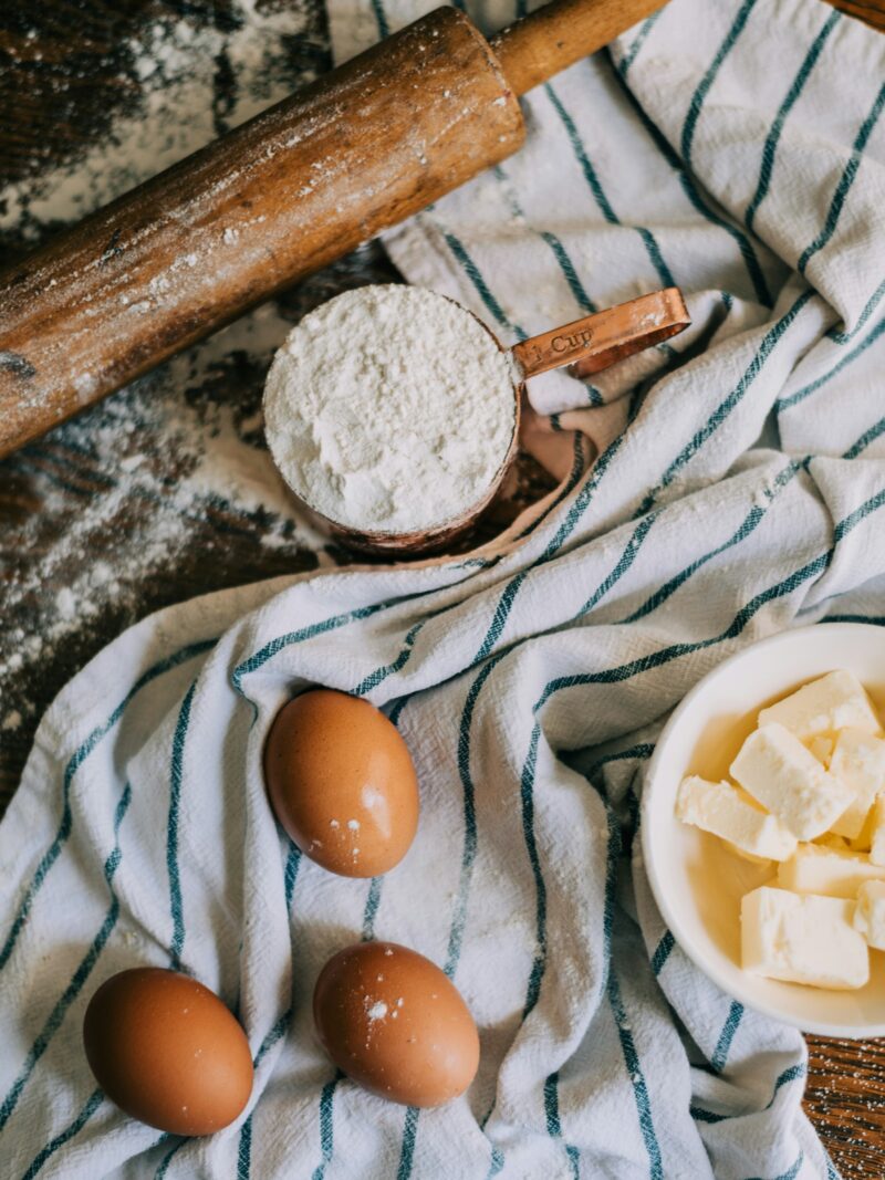 Flour, eggs and butter laid out on a linen-covered table for baking