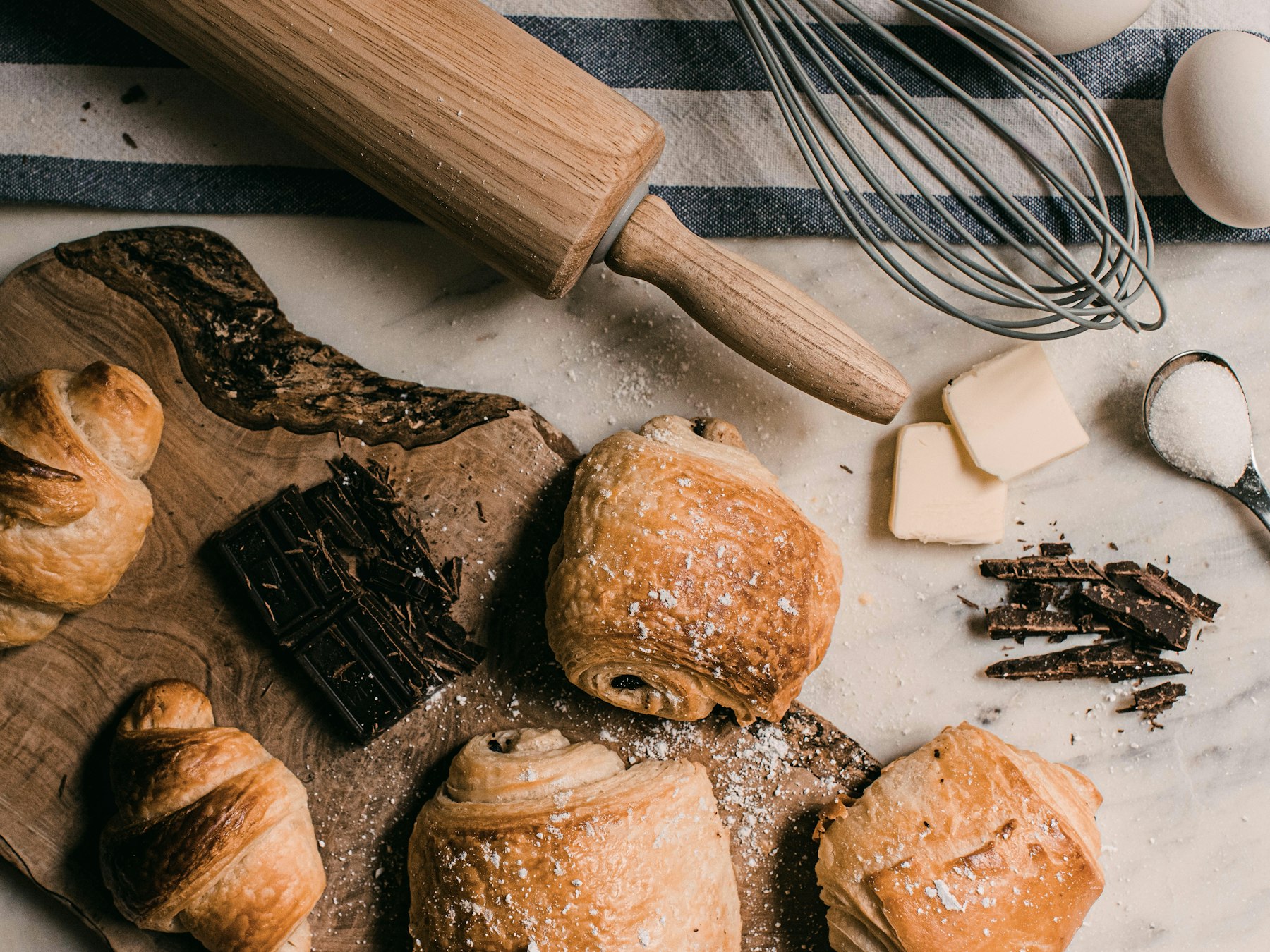 Freshly baked croissants and chocolate pastries on a wooden board with baking tools