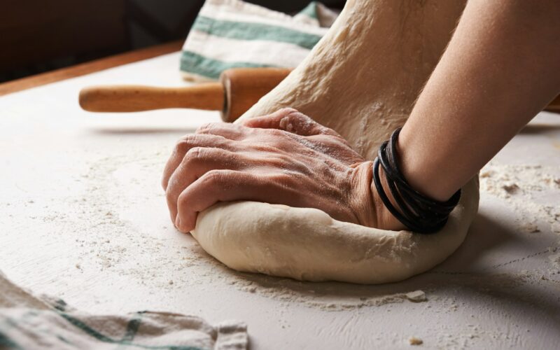 Hands kneading dough beside a wooden rolling pin