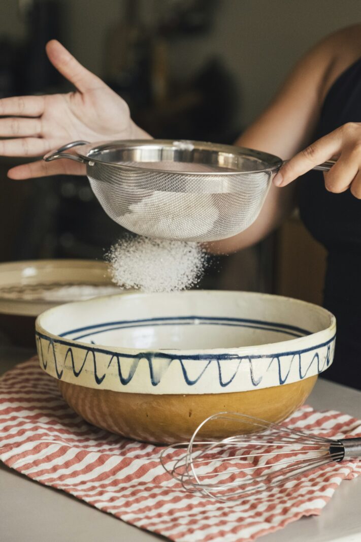 Flour being sifted into a ceramic bowl